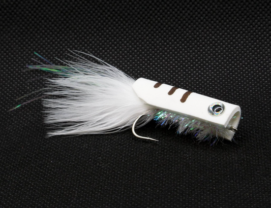 A white and green feathered fishing lure with a single hook, resting on a textured dark surface.