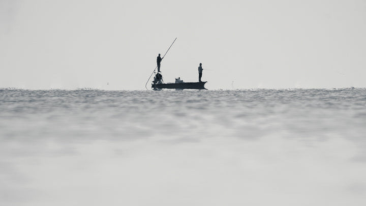 Person fishing from a small boat on a vast, fog-covered sea under a gray sky.