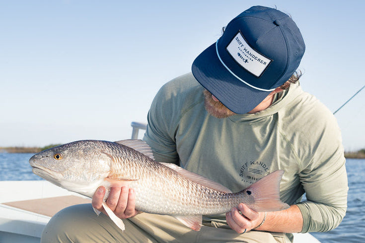 Man holding a large fish on a boat with a clear sky and water background