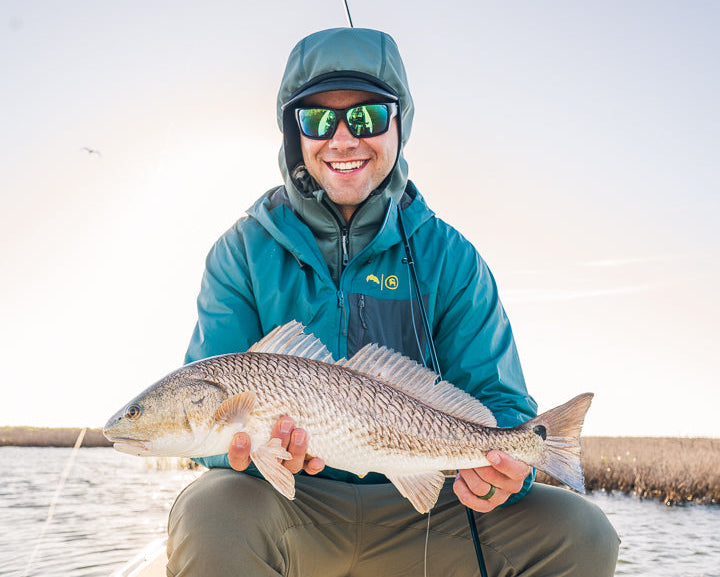 Man holding a large fish on a boat with water and sky in the background