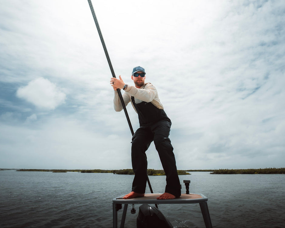 Man fishing from a small platform on a body of water with a cloudy sky.