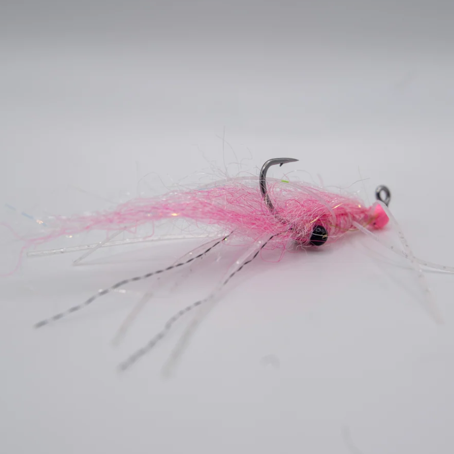 A pink fishing fly lure with a black bead eye, glitter fibers, and a silver hook, photographed on a plain light gray background.